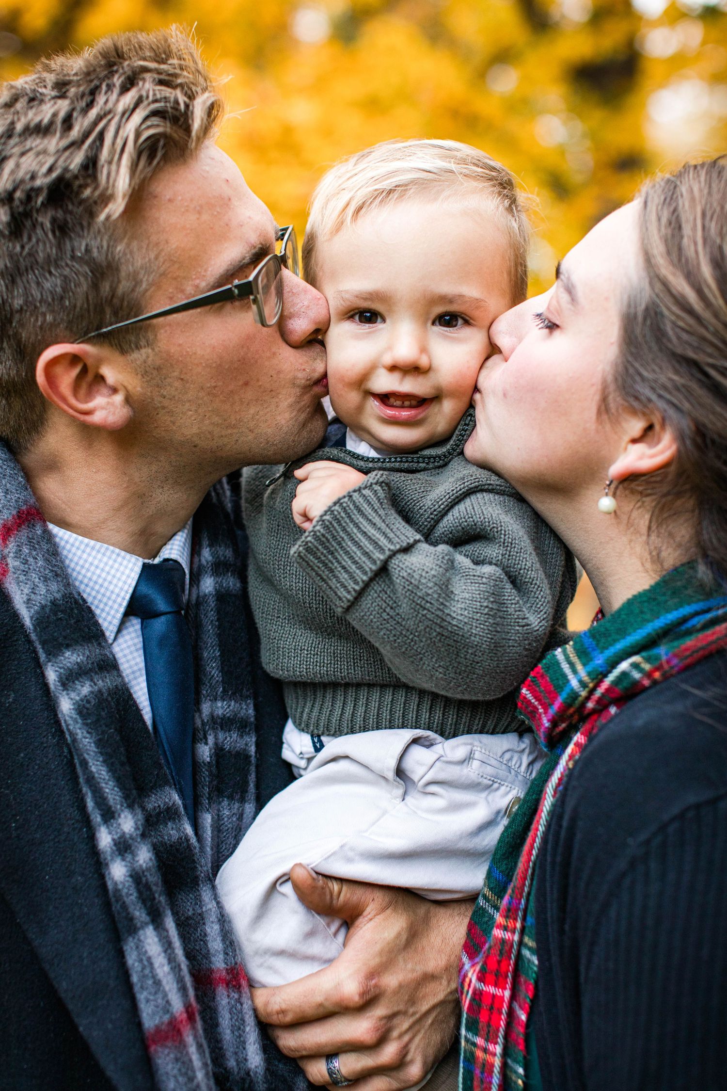 Family shares kisses and embraces against vibrant yellow fall foliage background.