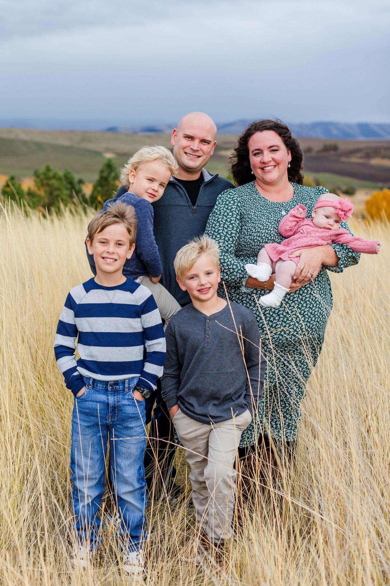 A family gathers in tall grass with mountains visible in the background during sunset.