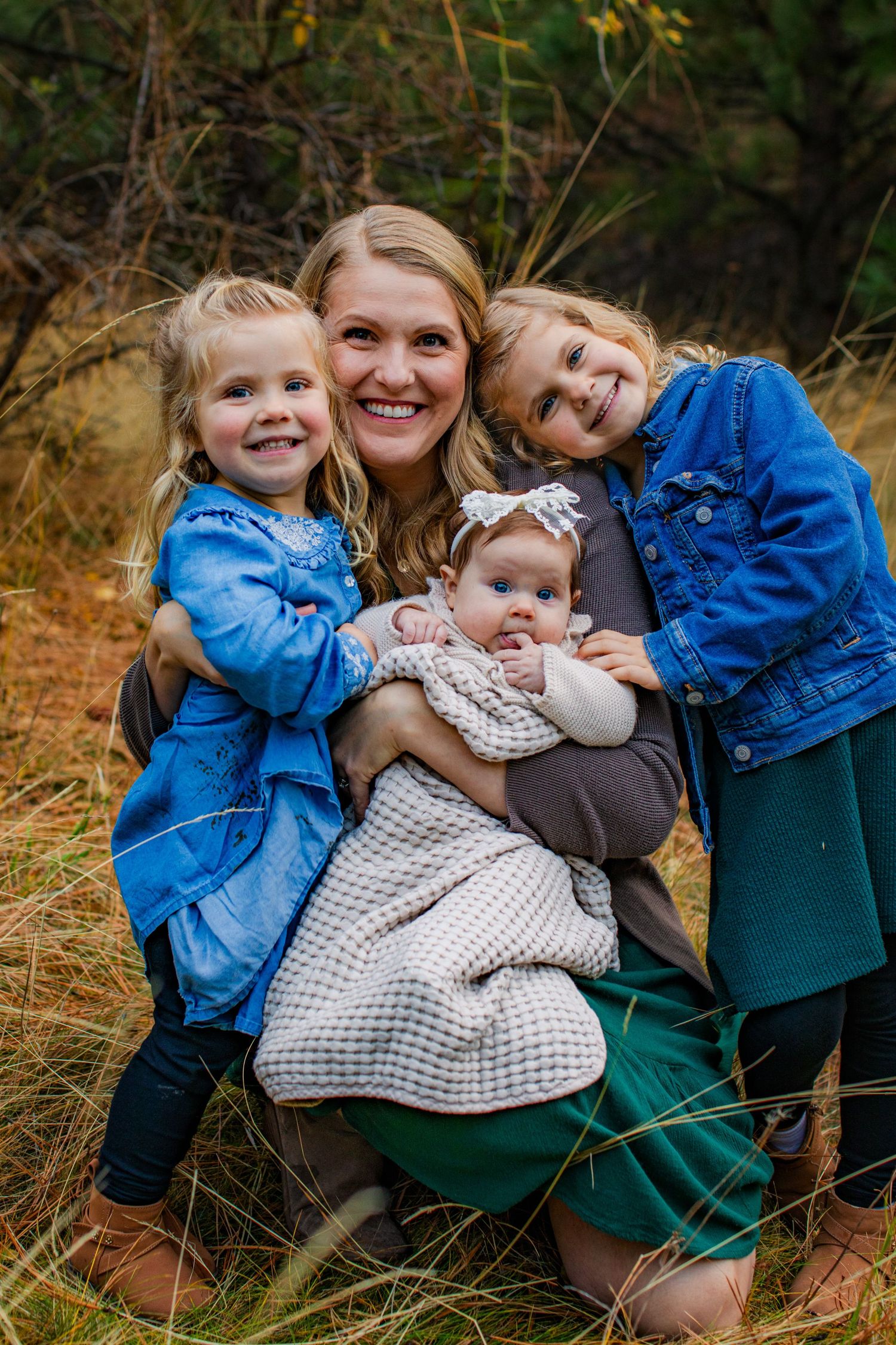 Family wearing blue denim and green sits together in autumn grass during outdoor photo session.