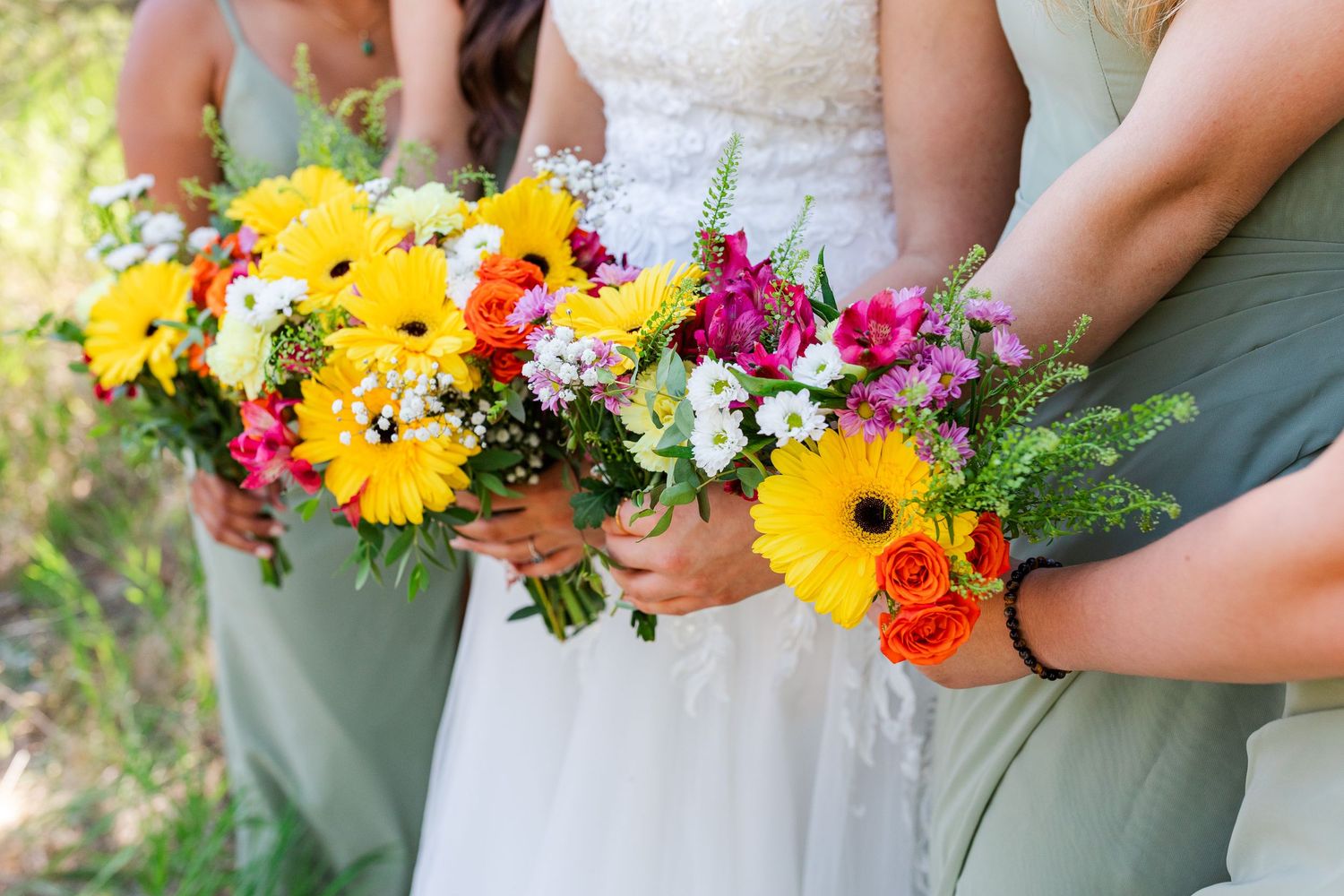 Vibrant bouquet of sunflowers and wildflowers held by hands in wedding attire.