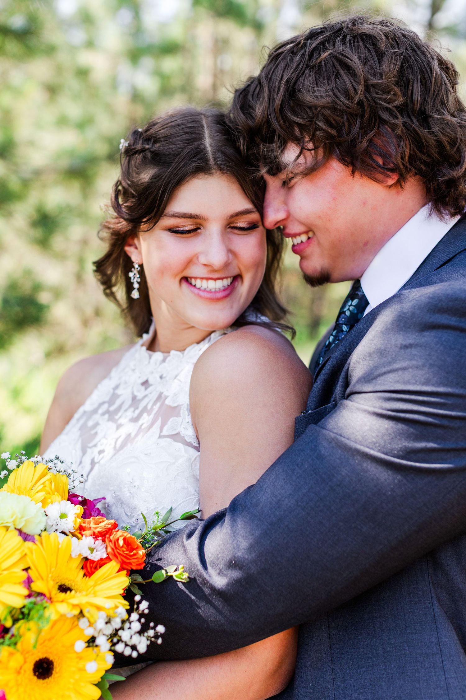 A couple embraces while holding bright sunflower bouquet during outdoor wedding photos.