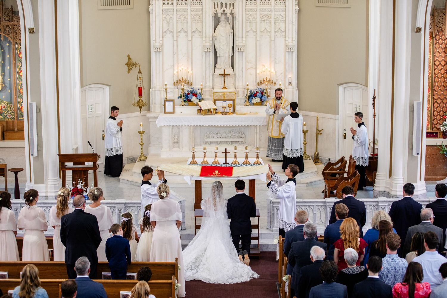 Traditional Catholic wedding ceremony at church altar with bride, groom, and attendants before priest.