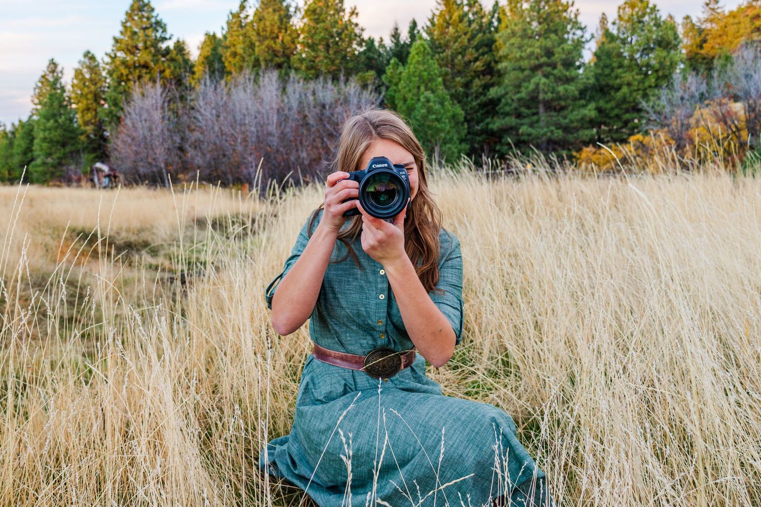 A photographer works with professional camera gear while positioned in tall autumn grass.