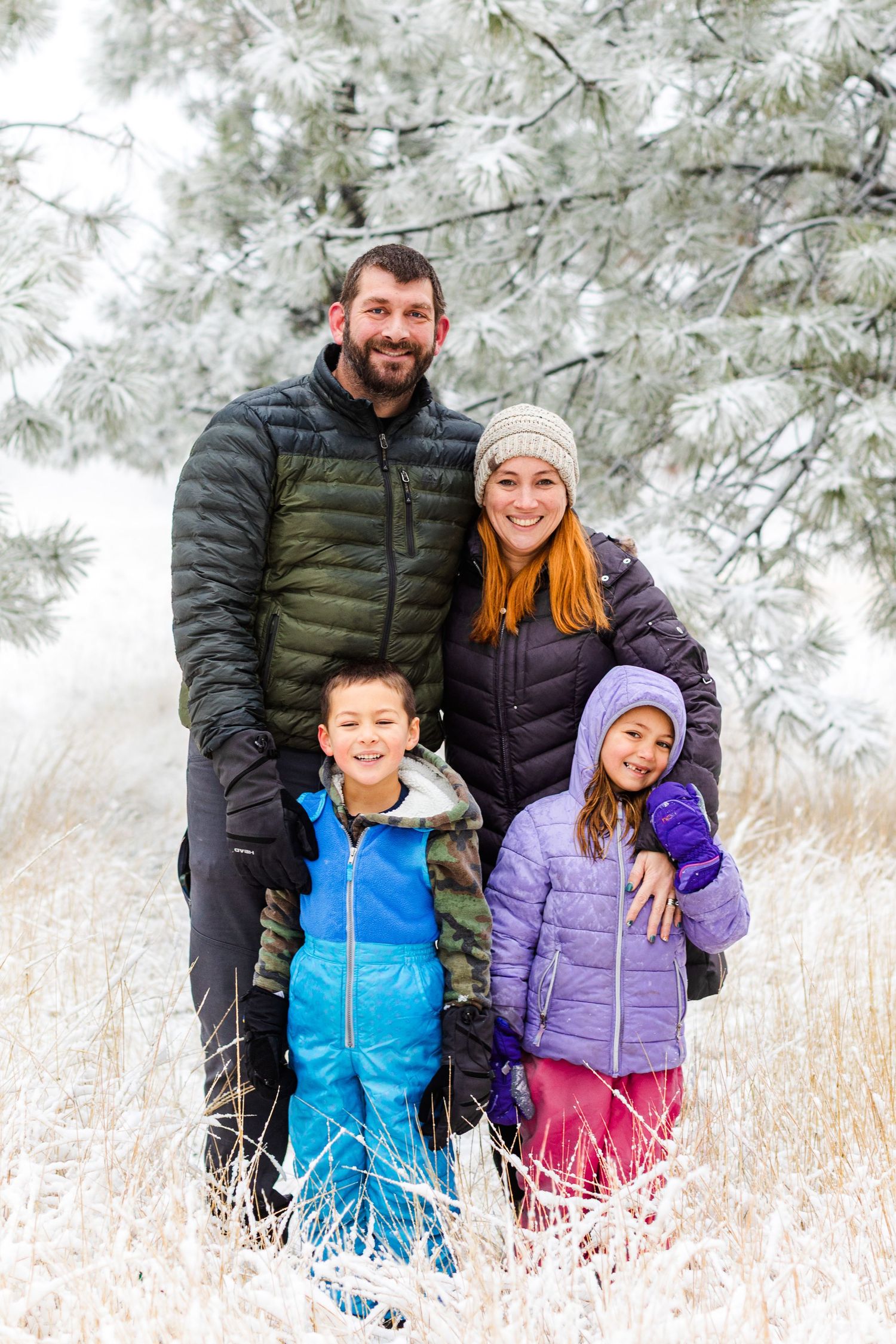 A winter family portrait with people wearing colorful puffer jackets posing together in the snow.
