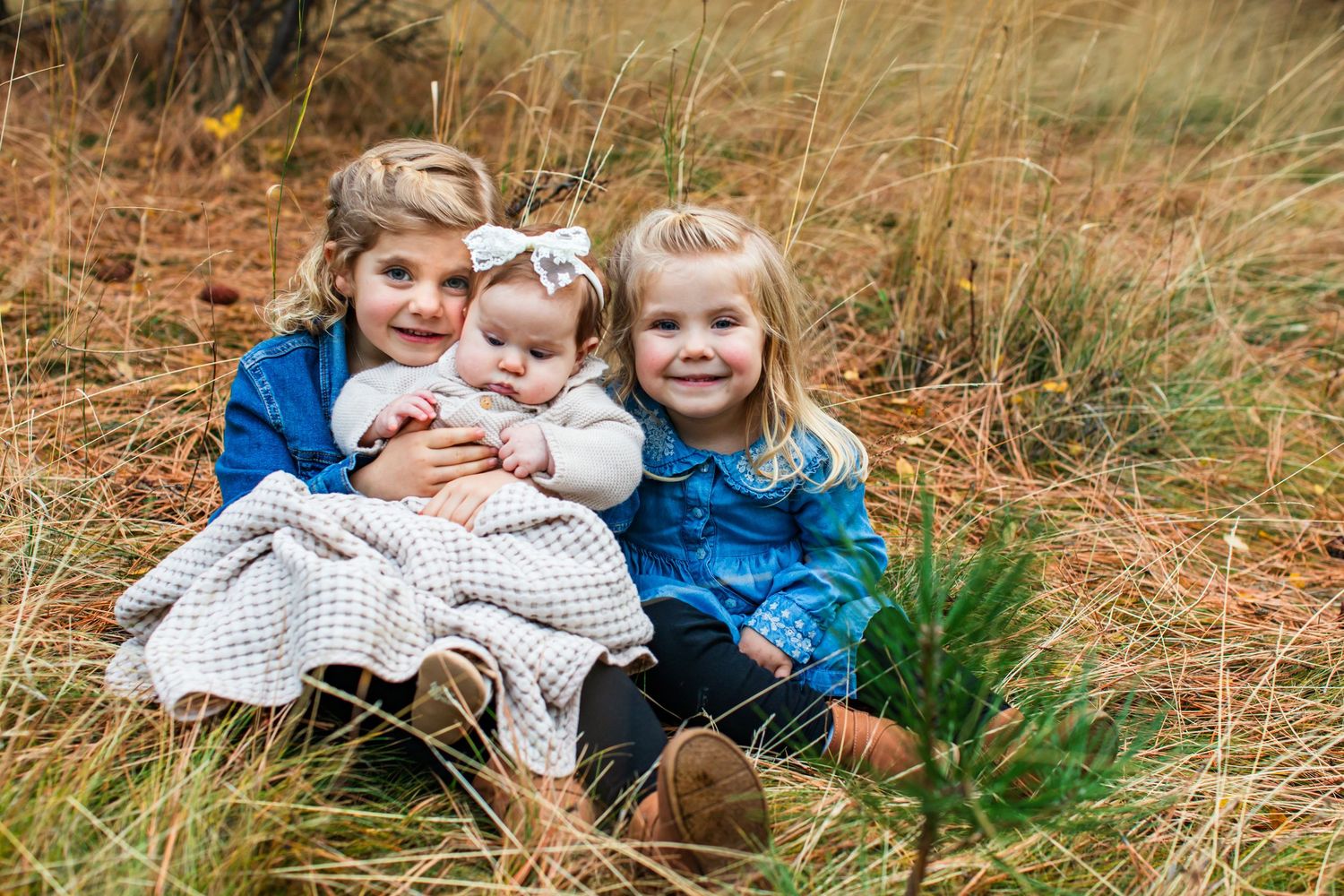 Three children in matching blue and white outfits sit together in a grassy field during autumn.