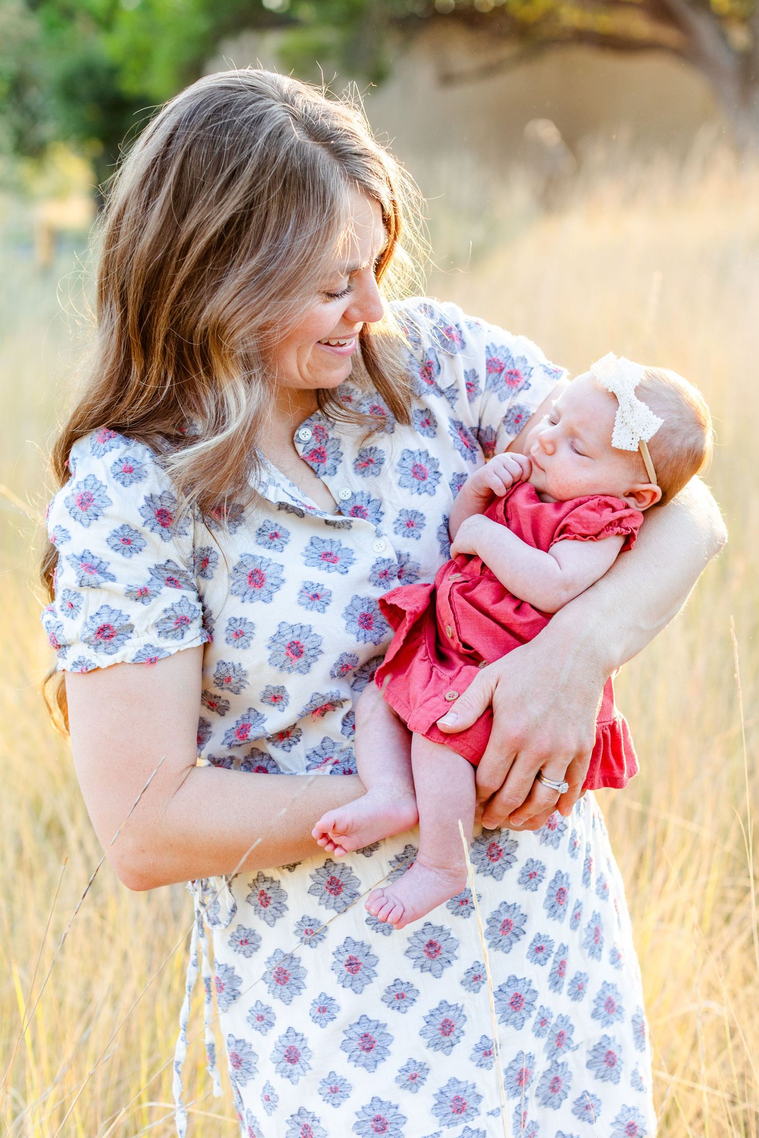 Woman in floral dress holding small child in pink outfit against golden sunset background.
