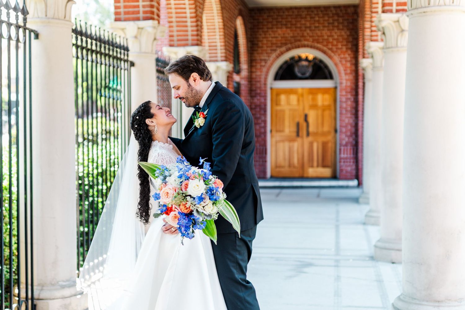 Bride and groom posing together in front of classic brick building with white columns.