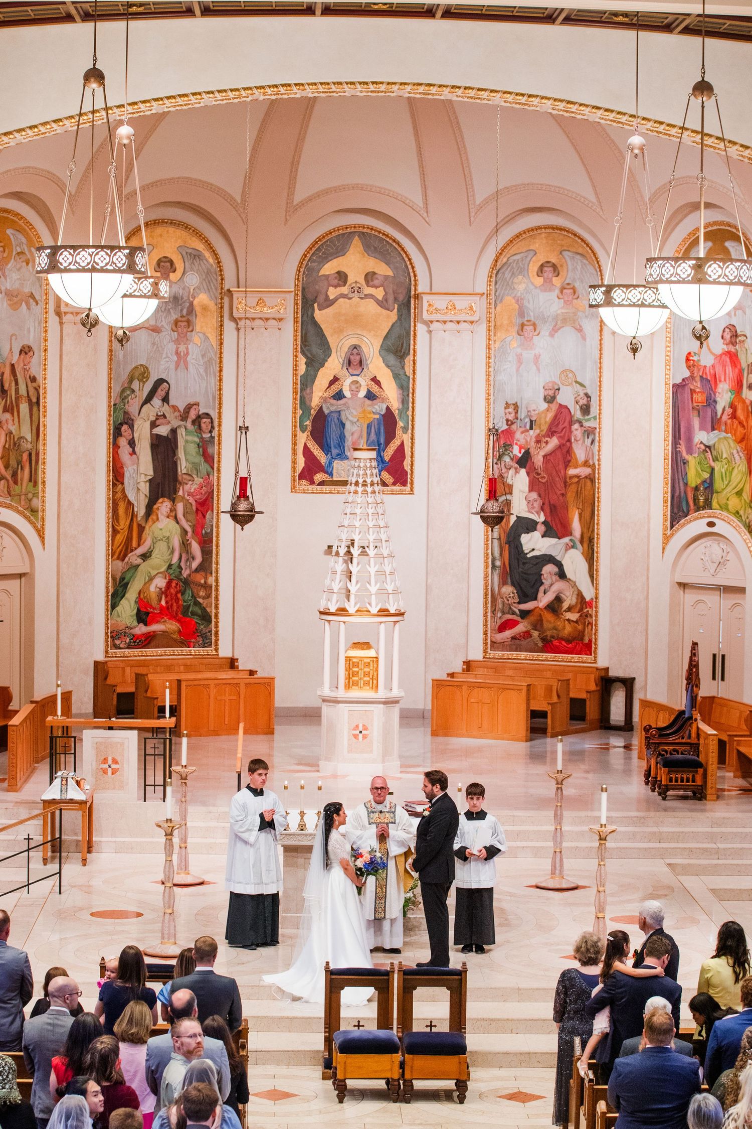 Religious ceremony taking place inside ornate Catholic church with stained glass windows and traditional altar decorations.