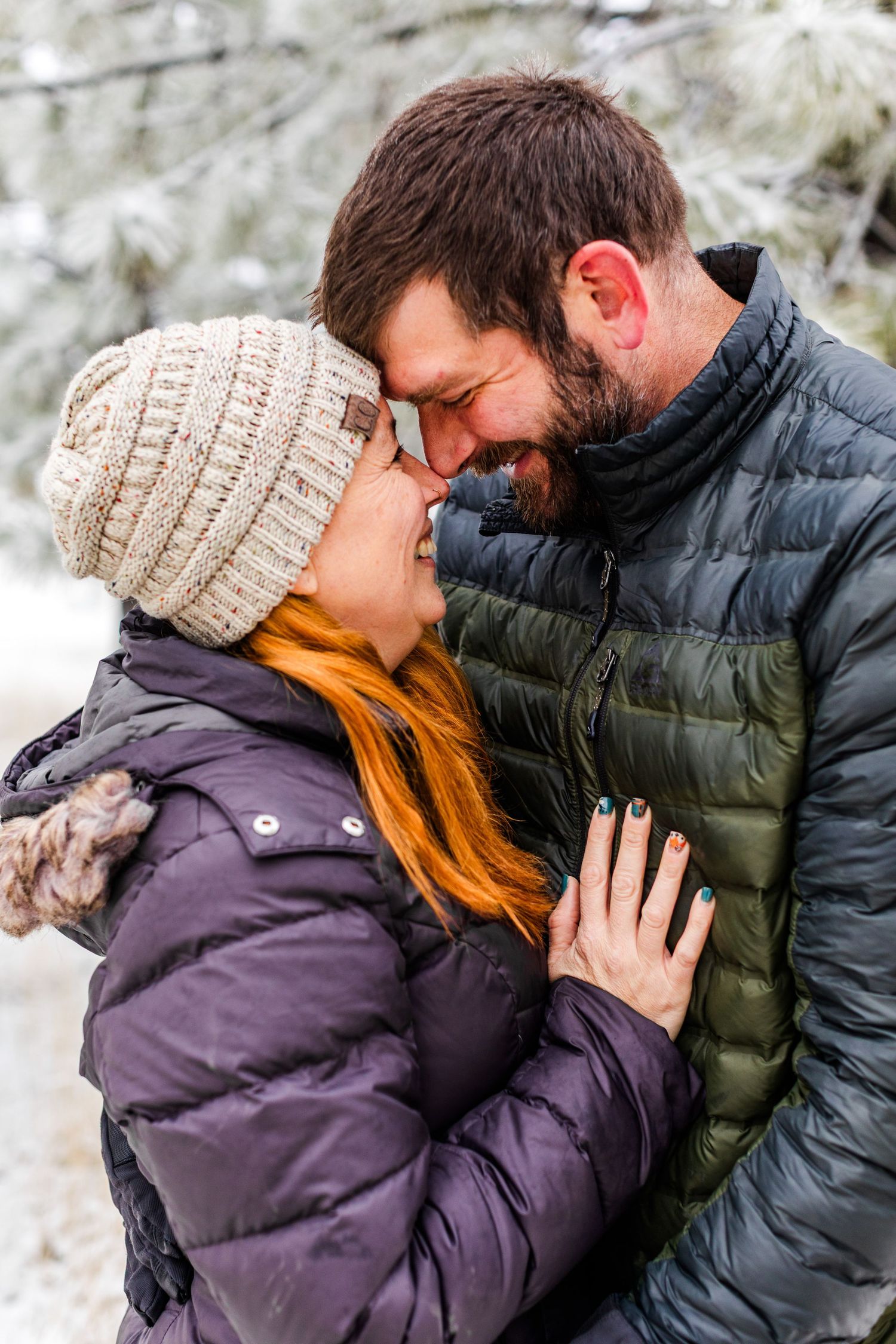 Couple sharing an intimate moment in winter clothing against a snowy backdrop.