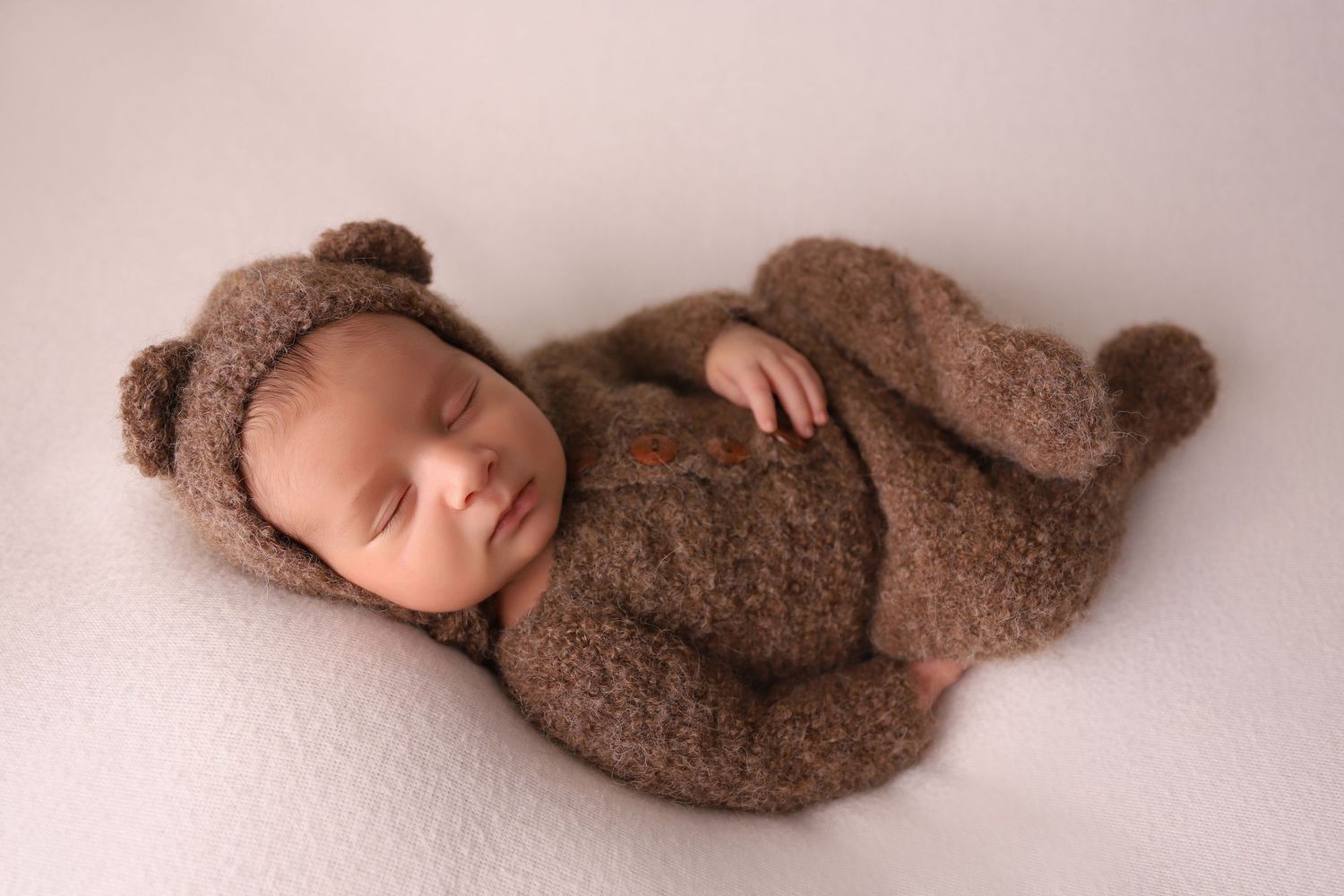 Newborn baby sleeping peacefully while wrapped in a soft brown swaddle blanket on a light pink background.