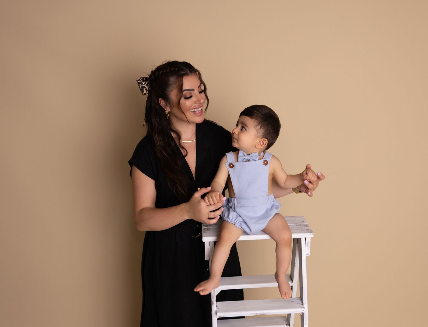A tender moment between parent and child as they interact on a white step ladder against a neutral backdrop.