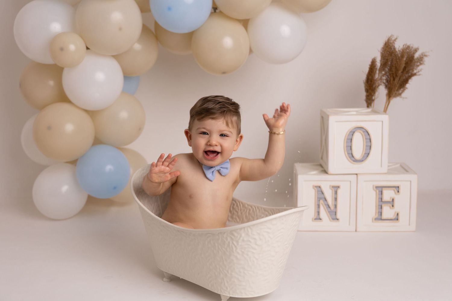 A series of cake smash photos with white and blue balloons against a neutral backdrop showing a milestone celebration.