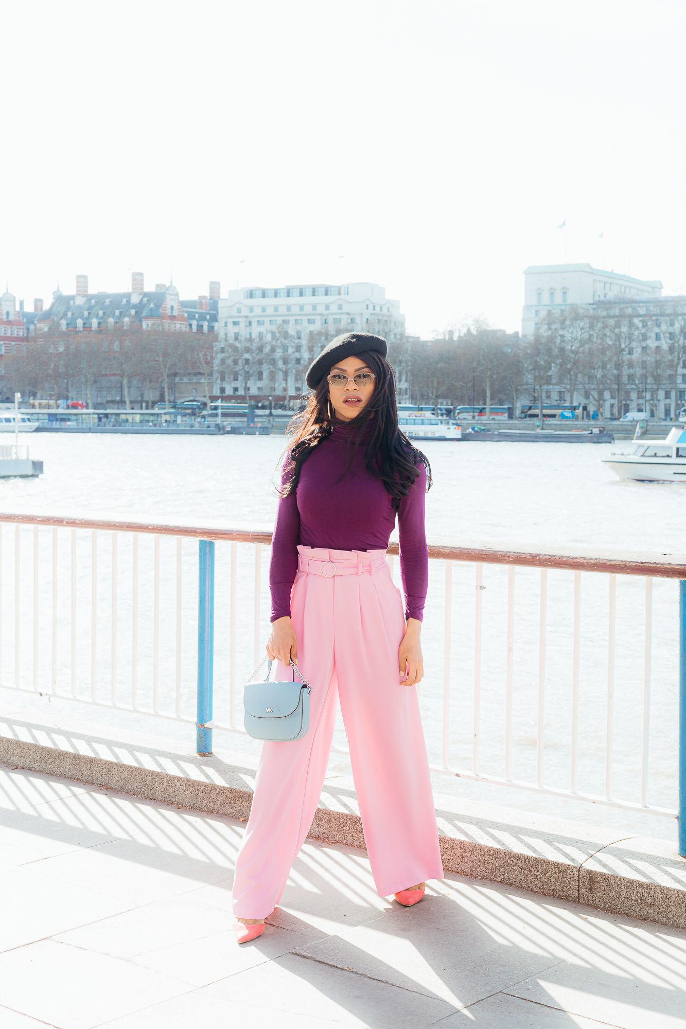 Stylish winter outfit featuring pink pants and purple turtleneck against urban waterfront.