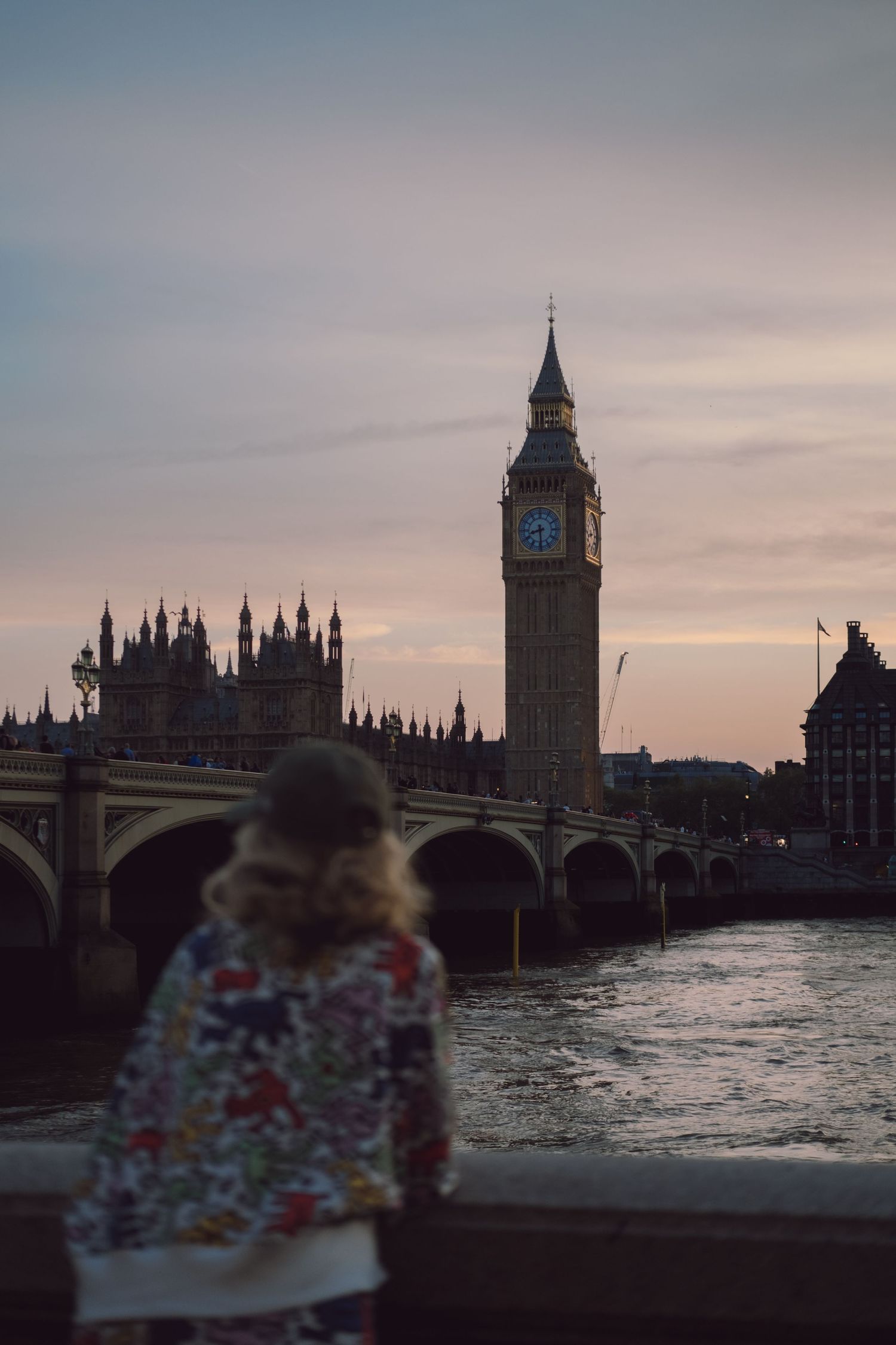 Person wearing patterned sweater views Westminster Bridge and Big Ben at dusk.