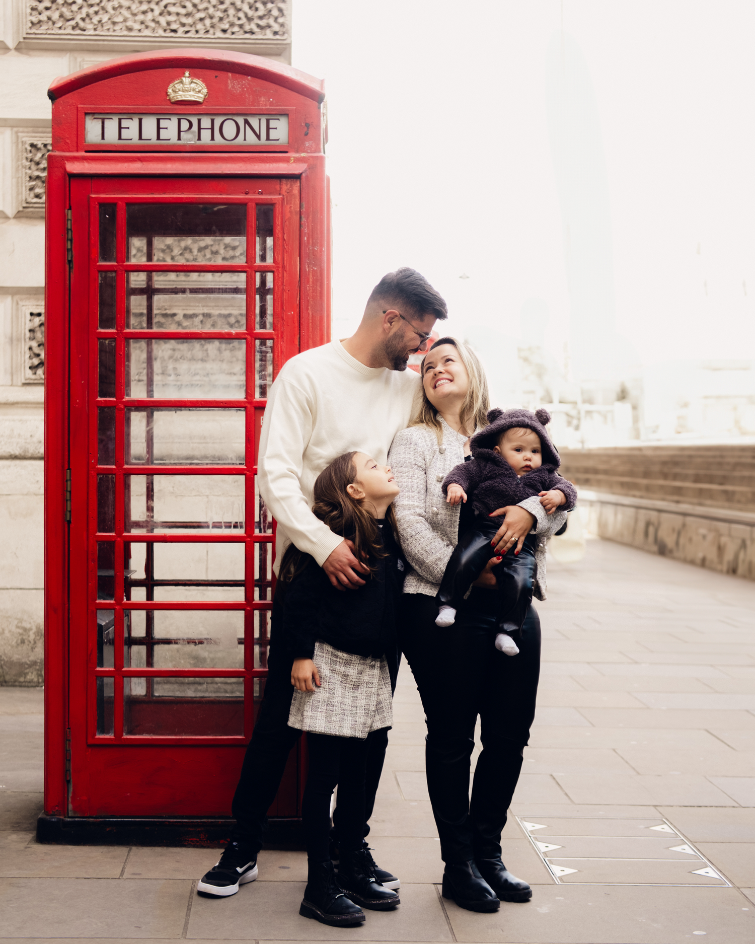 Family portrait next to classic red London telephone booth on city street.