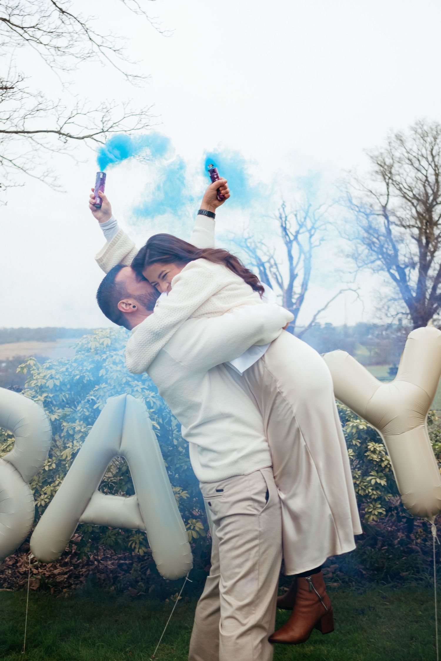 Wedding celebration with blue smoke bombs and decorative letters in an outdoor setting.