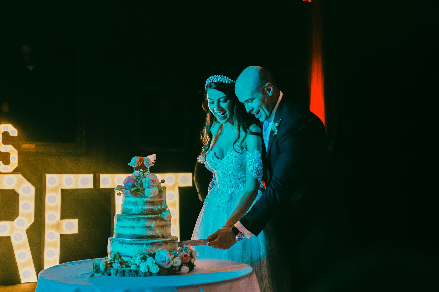 Couple admiring their wedding cake in moody blue lighting at reception.