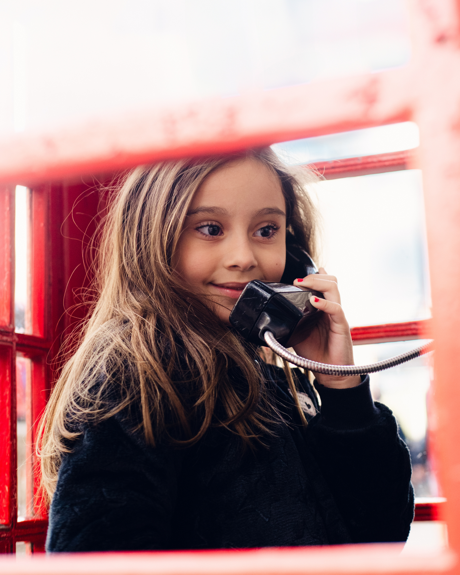 Young person using vintage phone inside traditional red British telephone box.