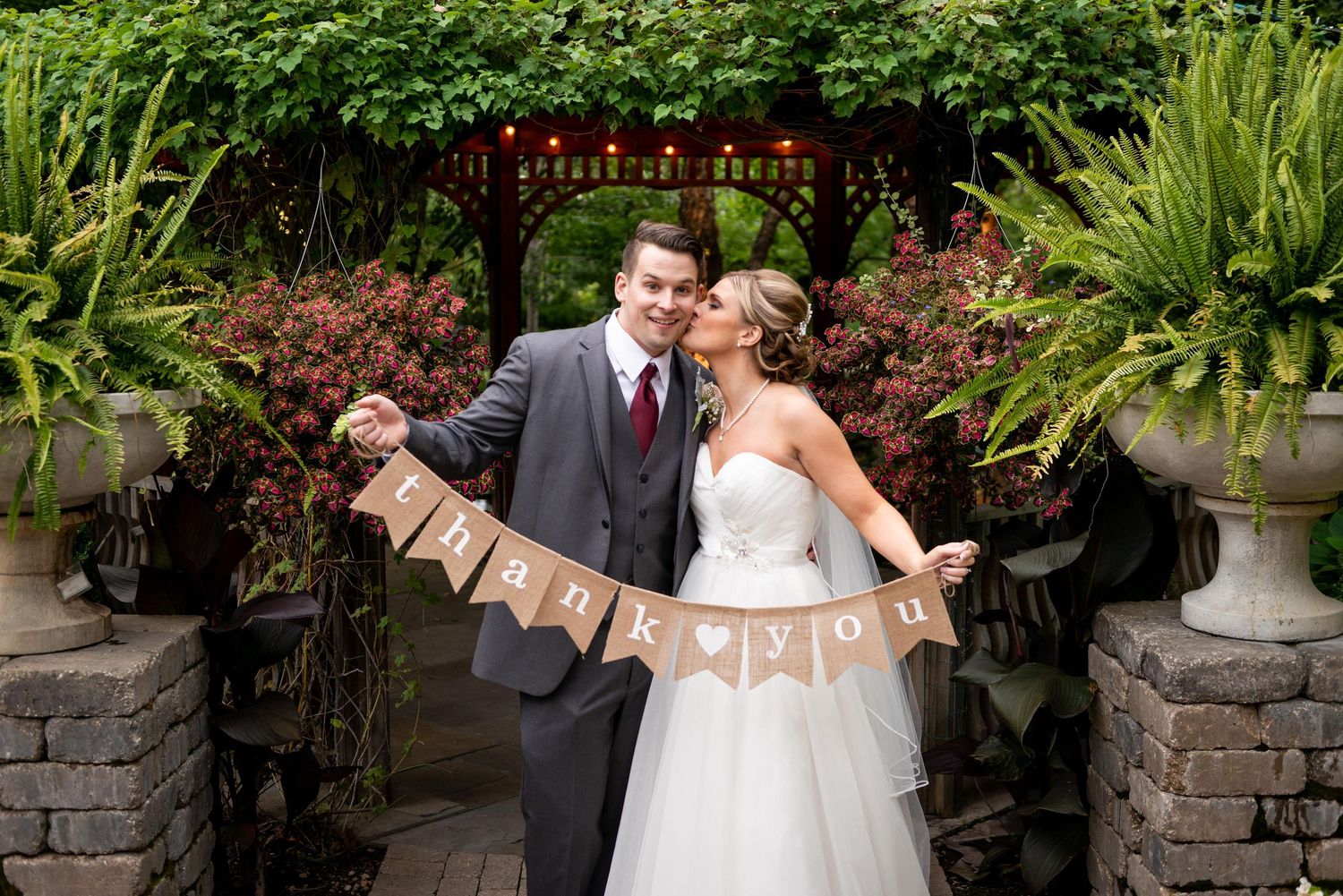 Wedding couple embracing in a lush garden setting with decorative banners.