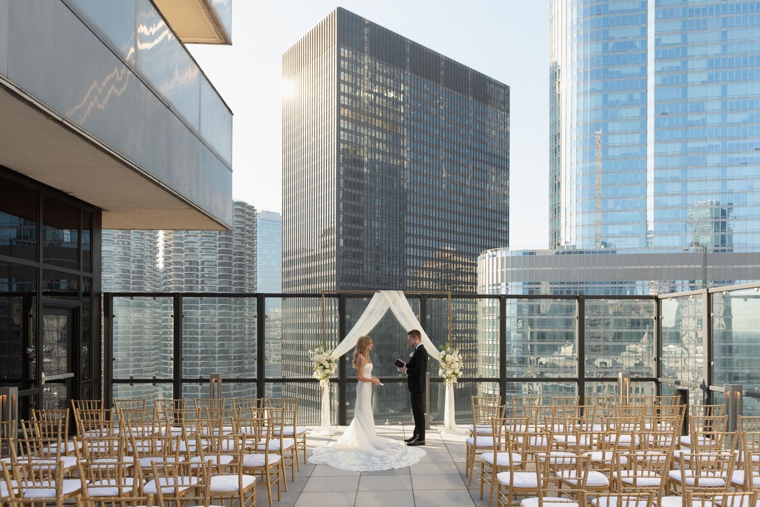 Outdoor rooftop wedding venue with rows of chairs set up for ceremony against urban skyline.