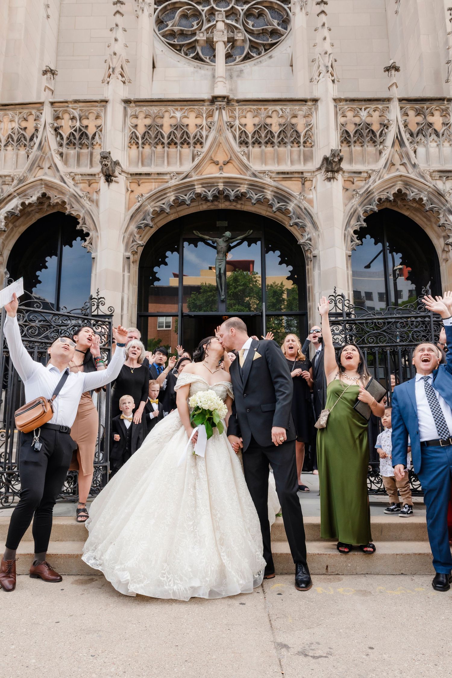 Wedding party celebrates joyfully outside Gothic architectural facade.