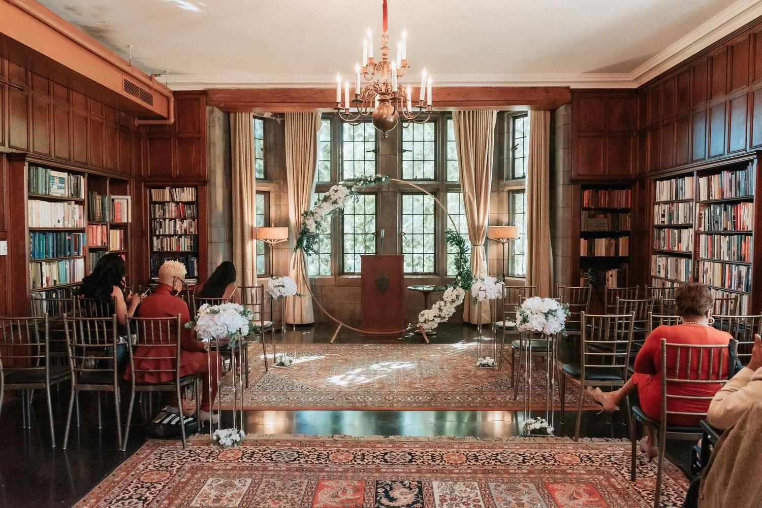 Elegant wood-paneled library room set up for a wedding reception with chandeliers and bookshelf-lined walls.