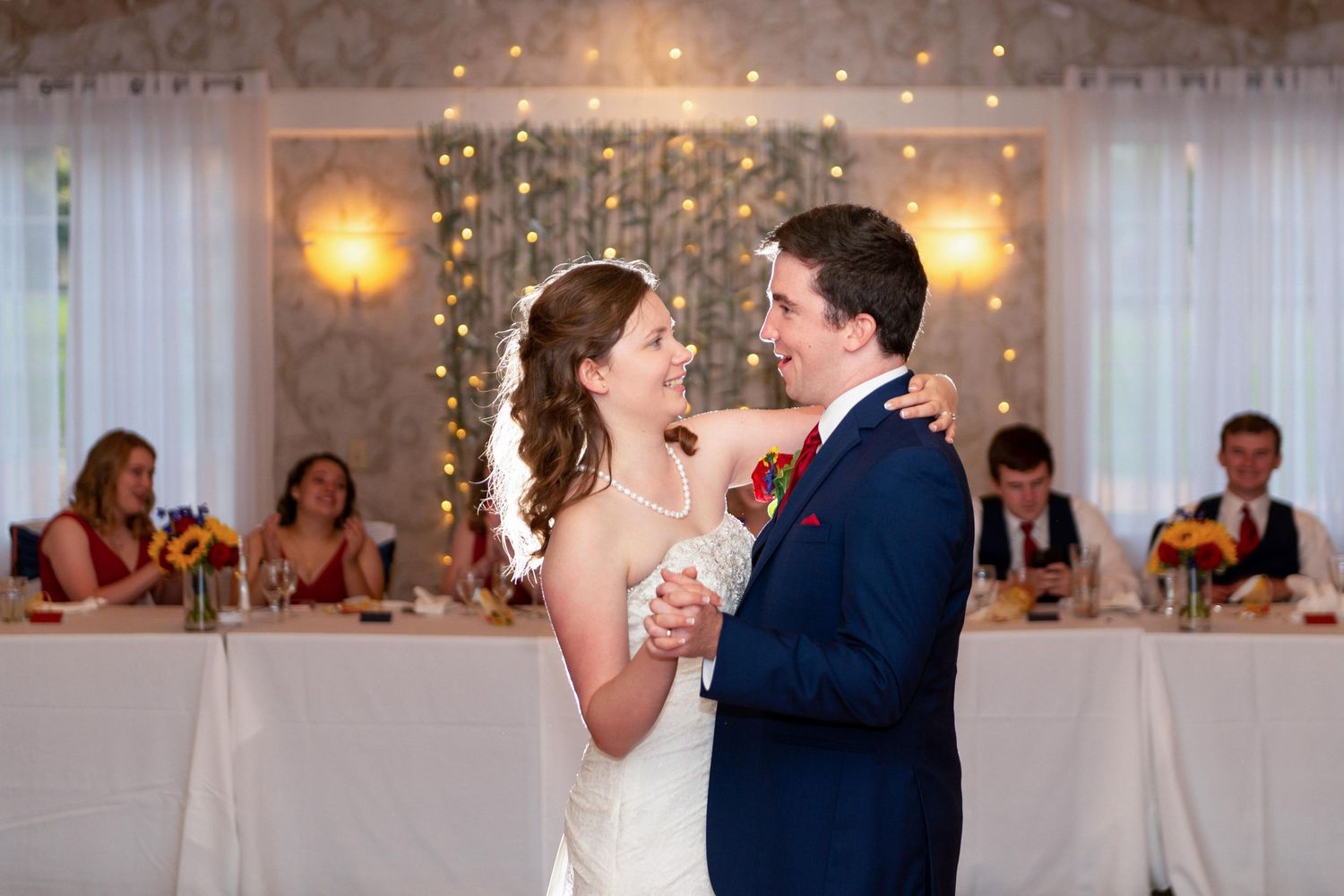 Wedding reception first dance with string lights and white draping in background.