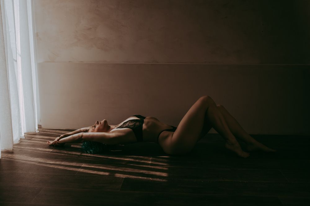 A shadowy figure lies on a wooden floor in dramatic light filtering through window blinds.