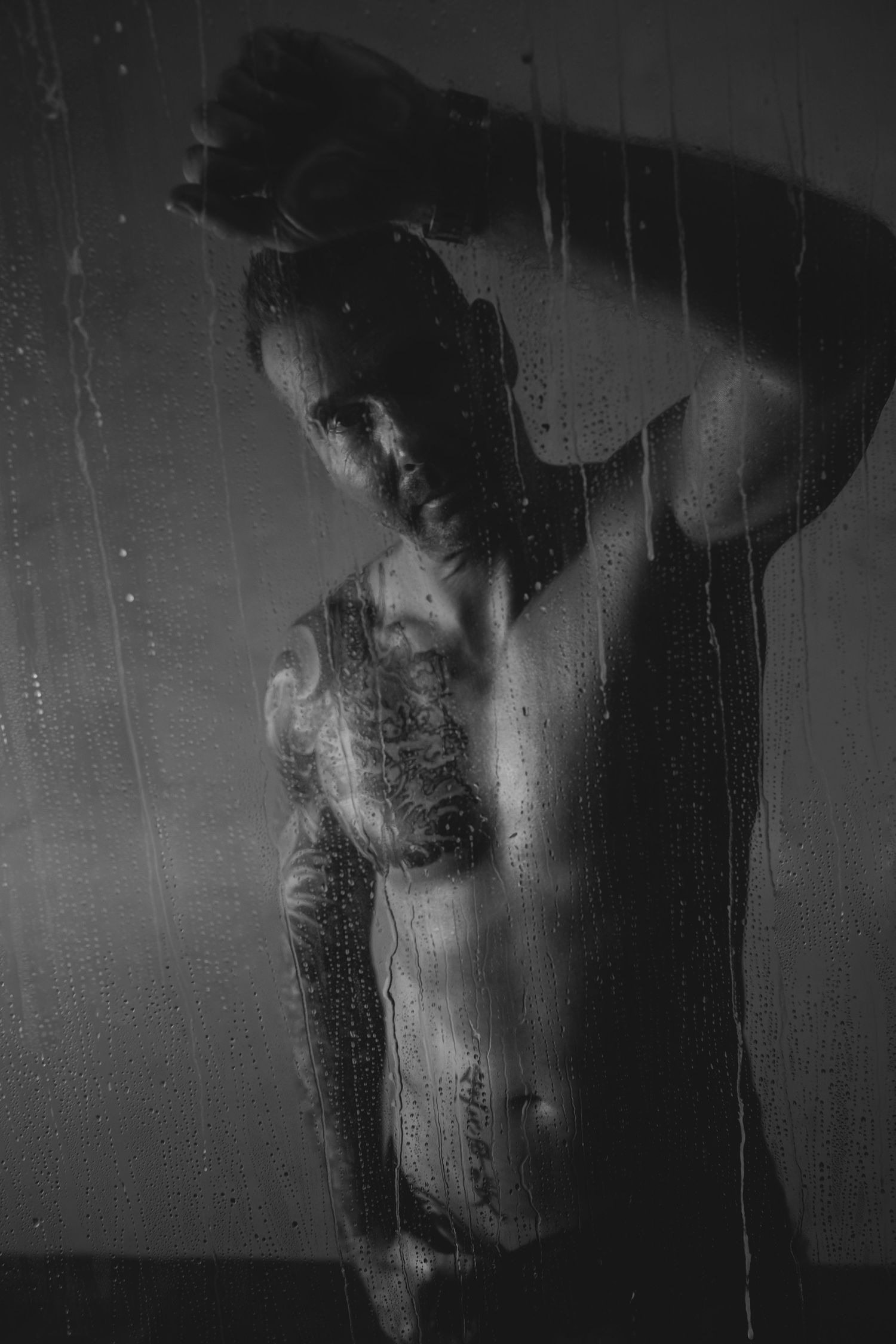 Mannenlichaam met een blote bovenlijf achter een douche met druppels die naar beneden vallen. Boudoir foto voor mannen, dudeoir