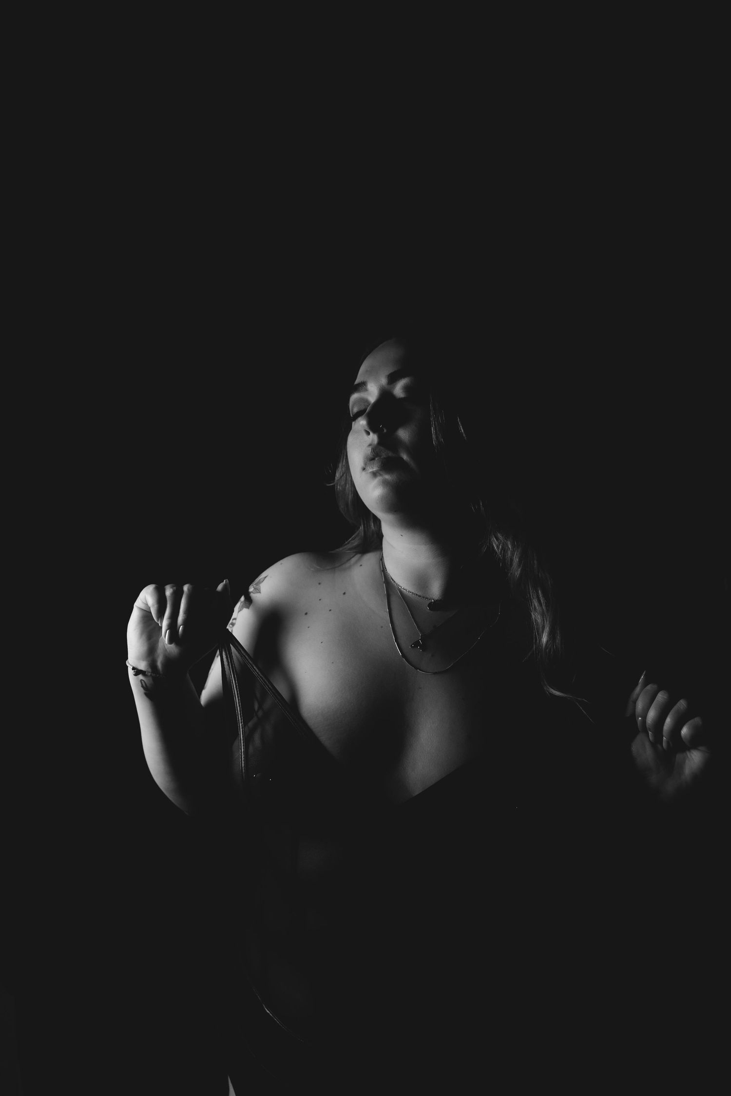 Black and white boudoir portrait of a woman with long hair posing dramatically against a dark background.
