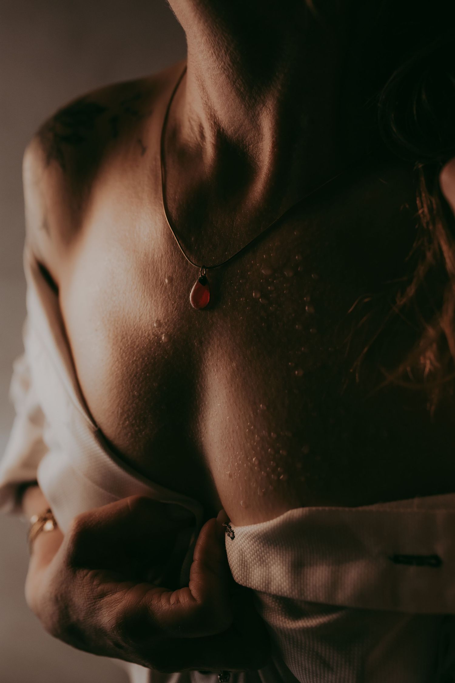 Close-up of a woman's freckled back wearing a red teardrop pendant necklace, partially draped in white fabric.