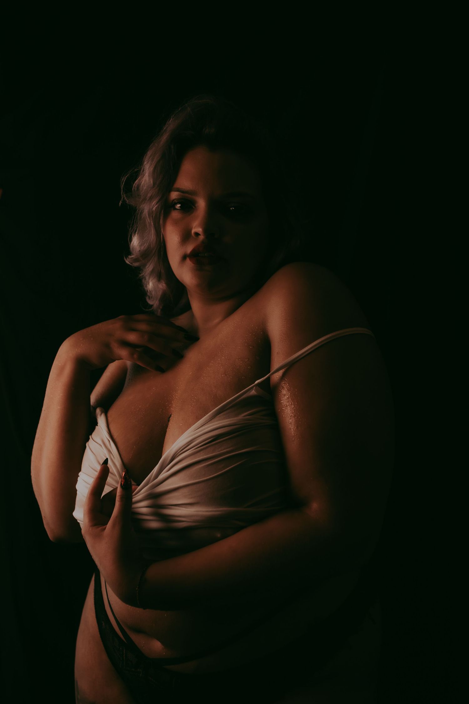 Artistieke boudoir foto met een vollere vrouw in een simpele wit t-shirt en een donkere achtergrond
