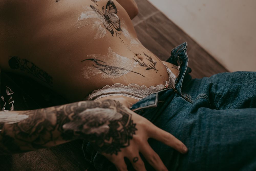 Close-up view of an arm with intricate floral tattoos wearing denim clothing in moody lighting.