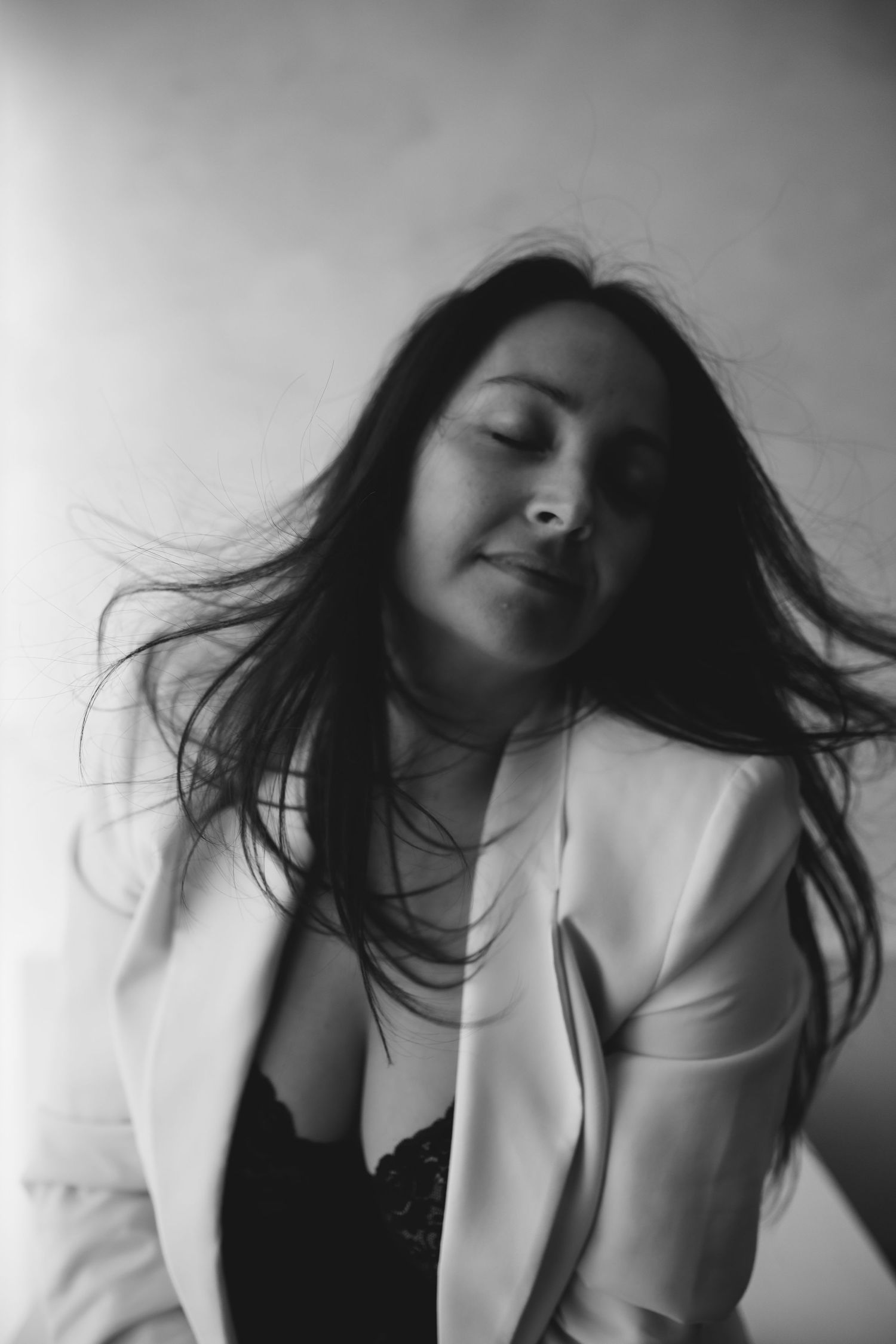 Black and white portrait of a woman in a white blazer with flowing hair and closed eyes.