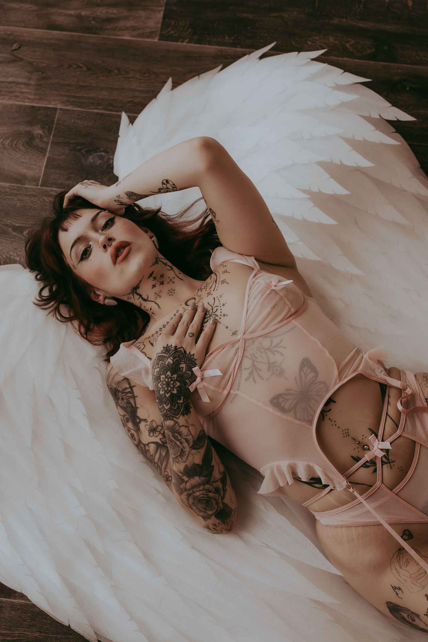 Vrouw met engelenvleugels liggend op de grond met een roze lingeriesetje met strikjes
