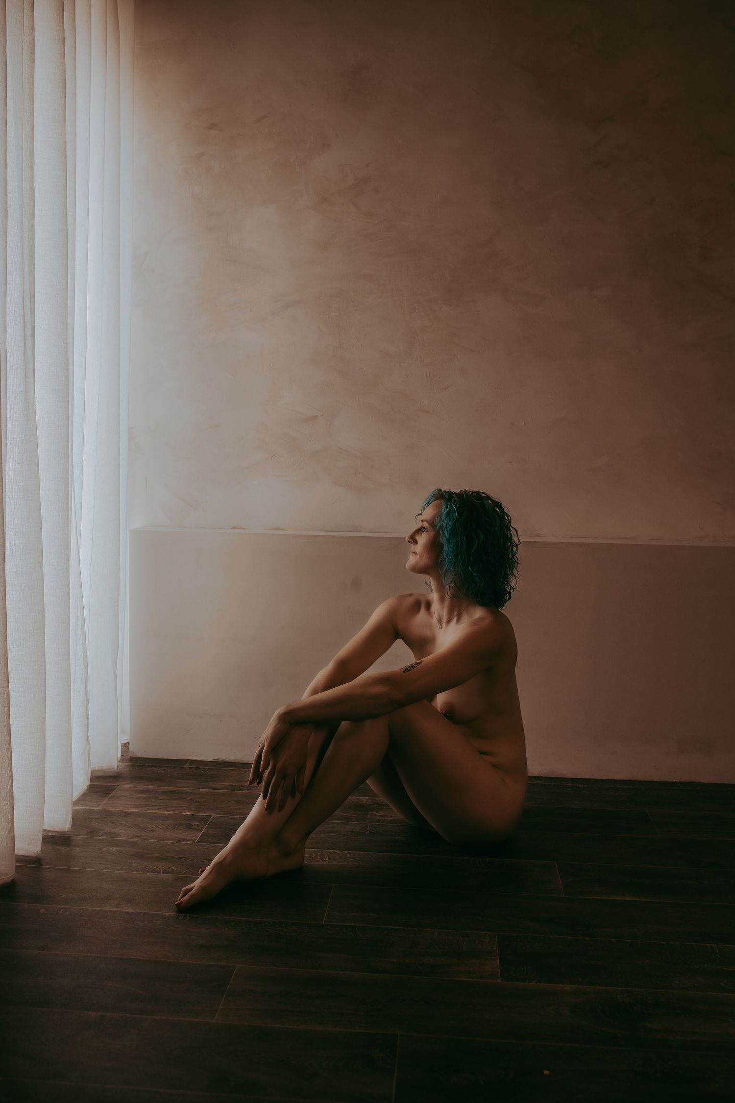 vrouw zittend op de grond met een naakte lijf en heel subtiel kijkend uit het raam