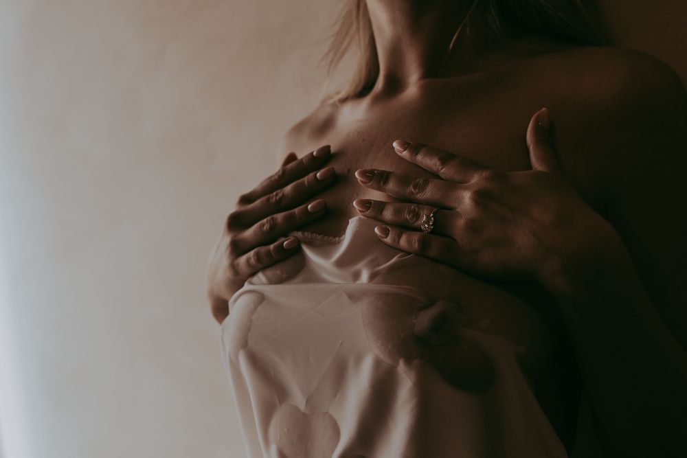 Person in white shirt holding chest with ringed hands in soft, moody artistic portrait photography.