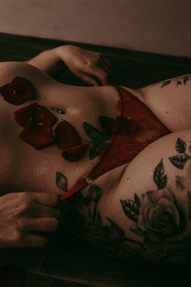 Artistic dark moody boudoir photo with rose tattoos and red lingerie in shadows creating sensual atmosphere.