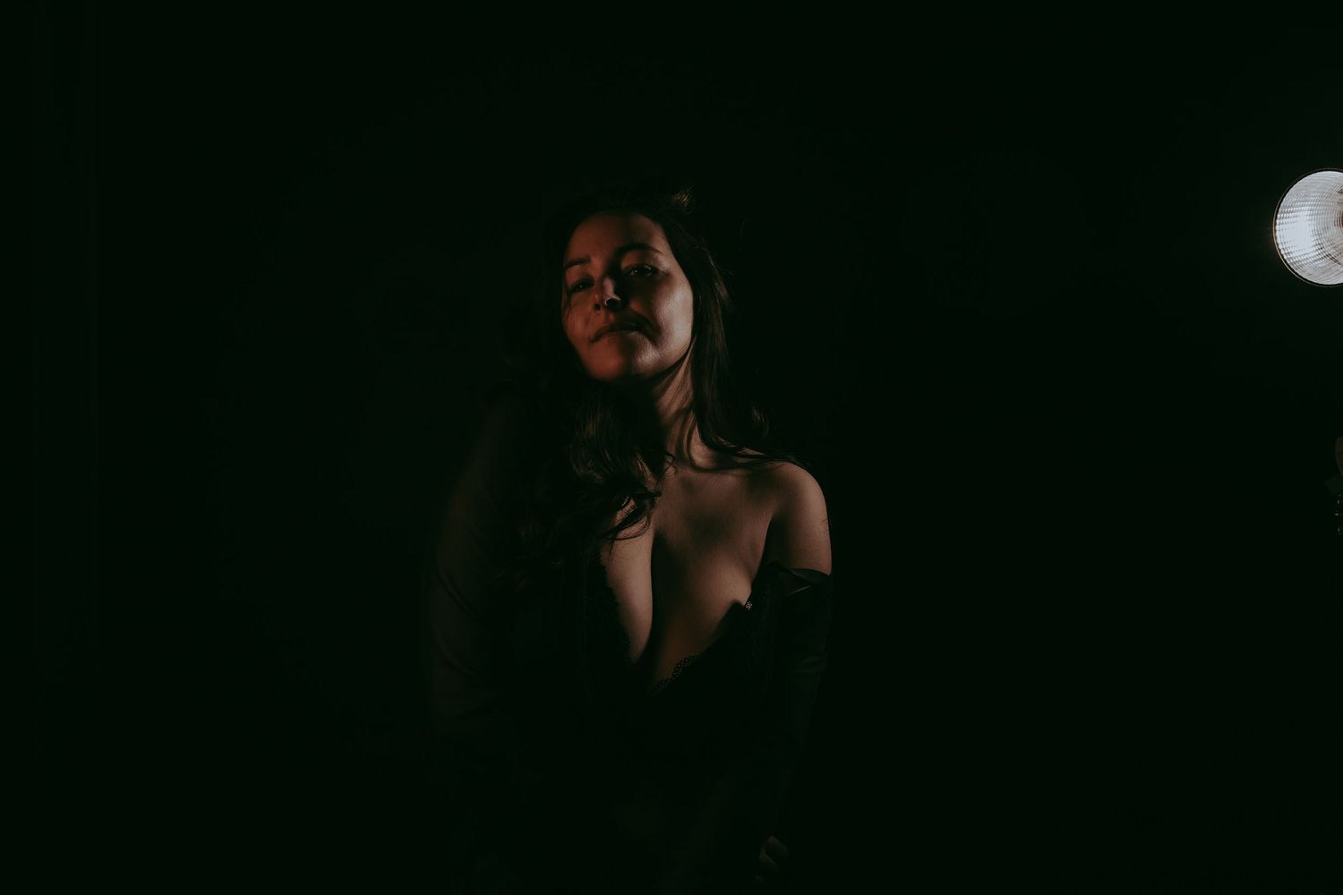 A woman poses dramatically in low-key lighting against a dark background with a moon visible behind her.