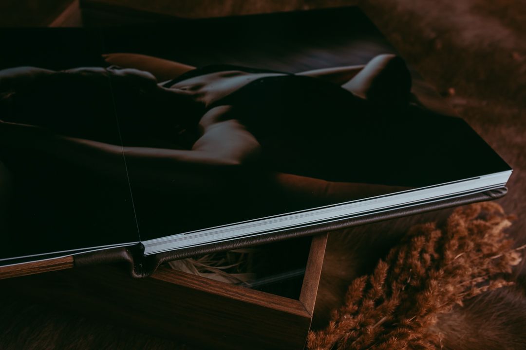 A dark leather photo book resting on a wooden box with dried florals, showcasing elegant black cover design.