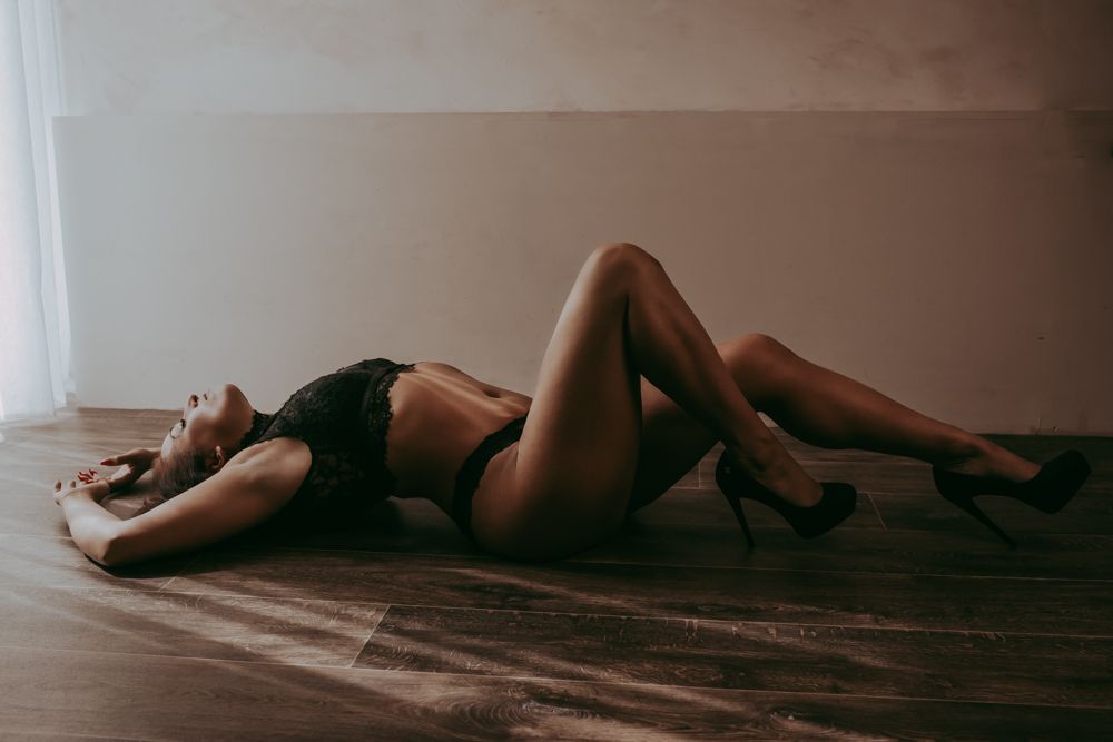 Woman in black lingerie lying on hardwood floor in moody boudoir photography session.