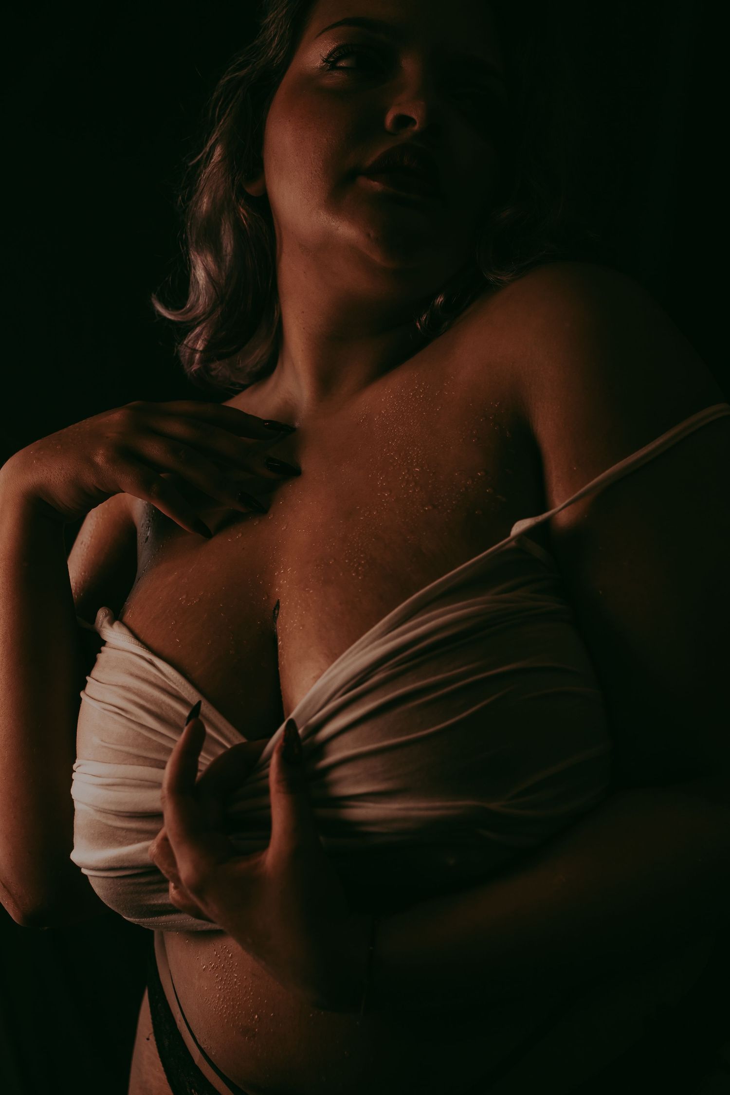 Moody boudoir foto van een vrouw met een maatje meer met een donkere achtergrond en een wit t-shirt