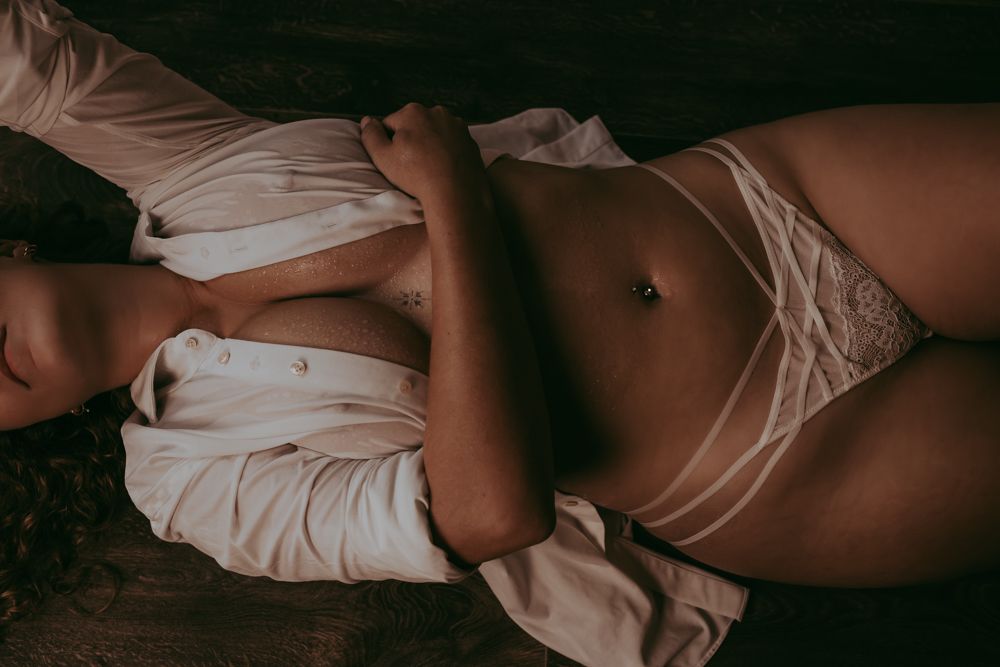 Intimate boudoir photography of a feminine figure in white lingerie lying on dark wood flooring.