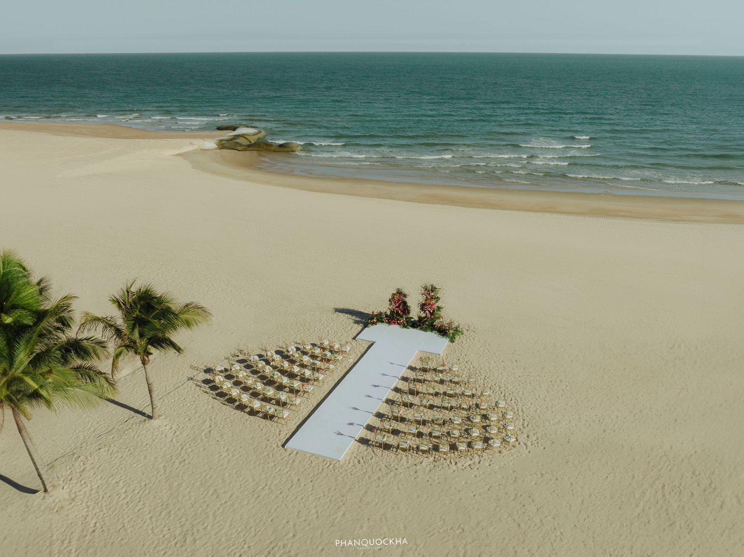Aerial view of a beautifully arranged beach wedding ceremony setup with chairs near the ocean.