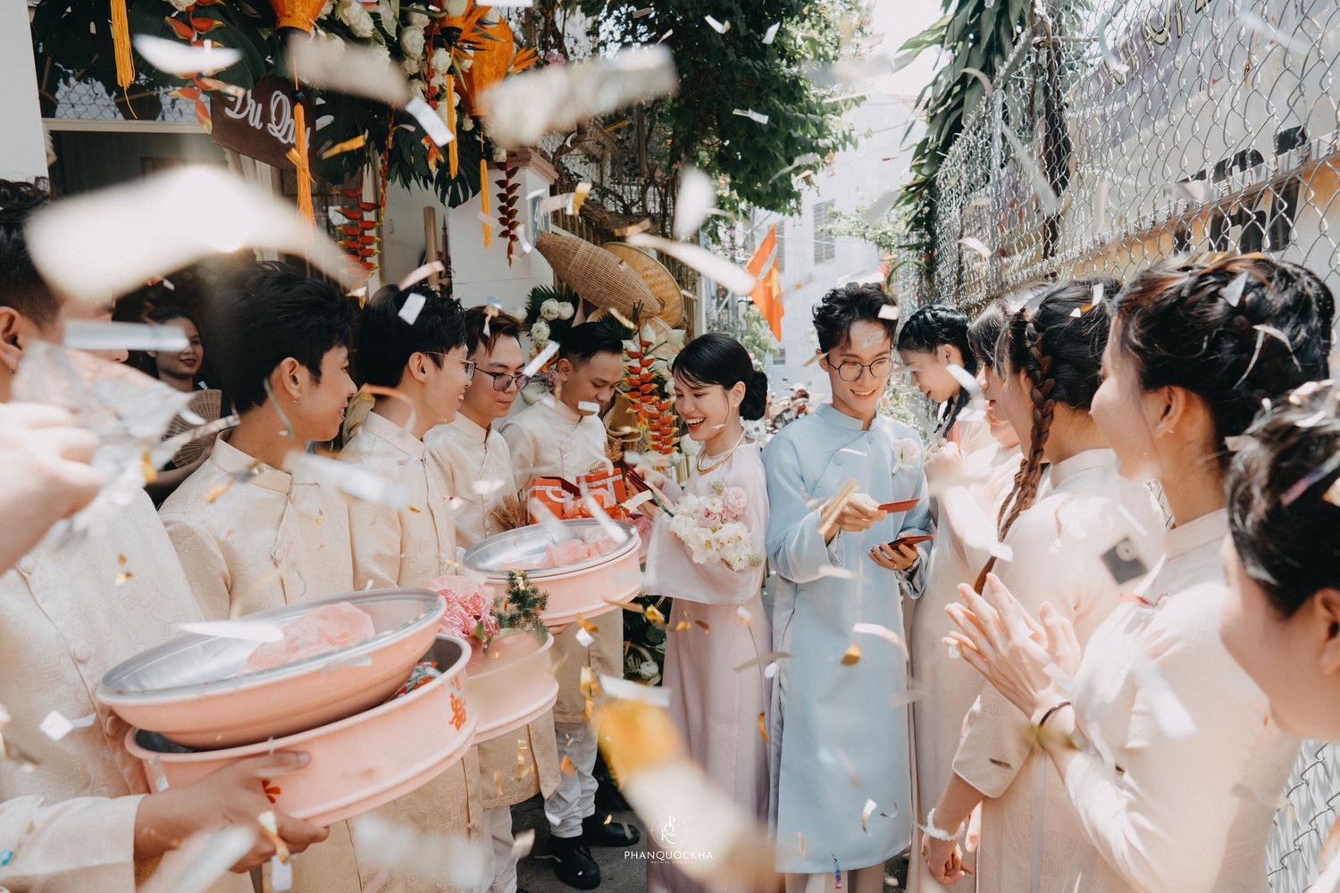 Joyful wedding procession with confetti, guests in traditional white attire celebrating outdoors.