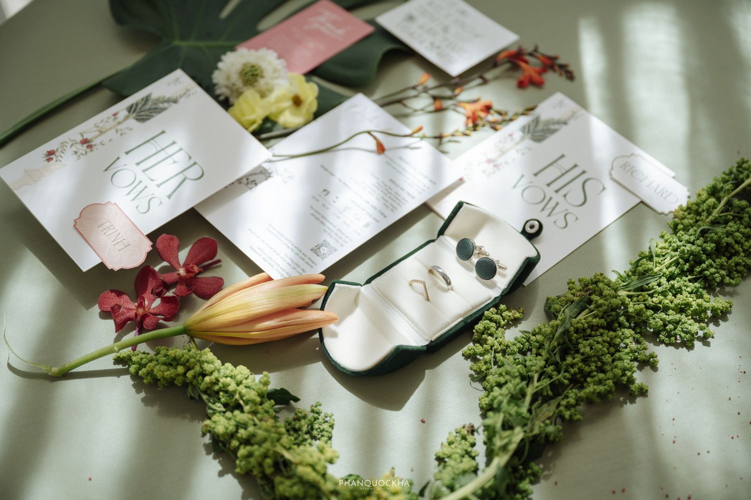 Flat lay of wedding stationery, jewelry, and tropical flowers arranged on a light surface.