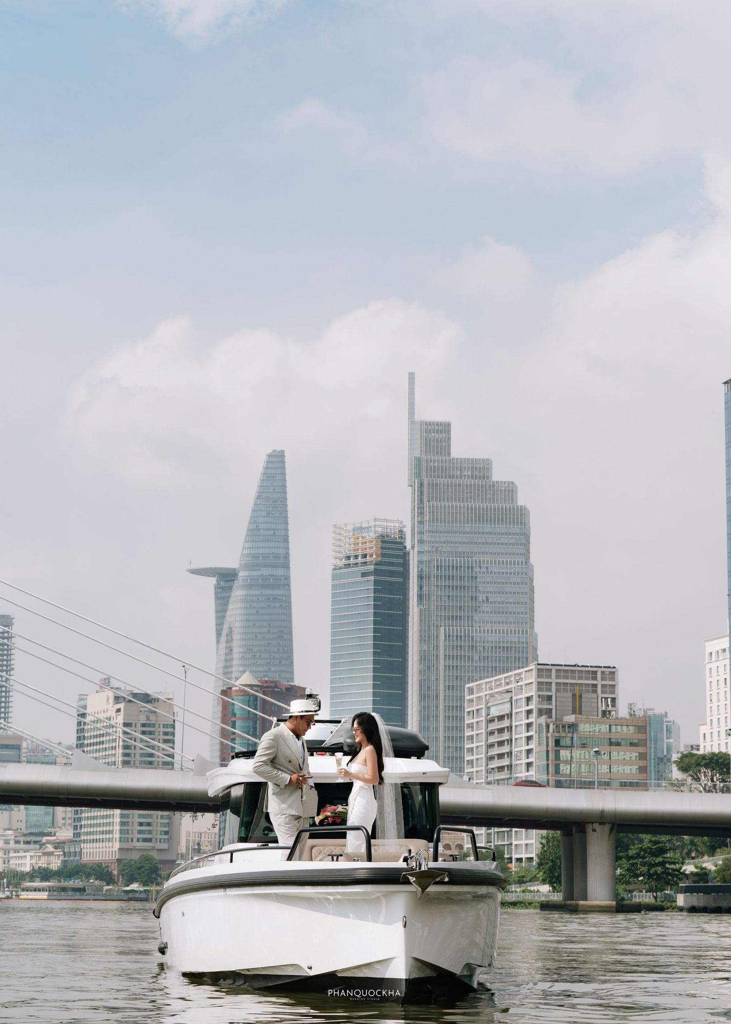 Couple posing on a luxury white motorboat with a modern city skyline in the background.