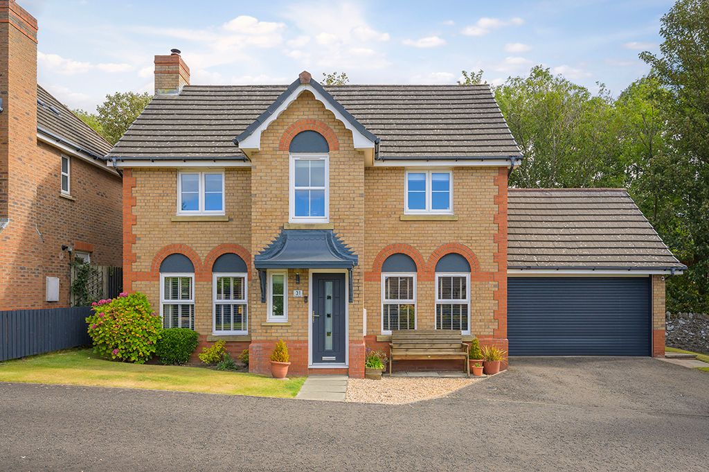 Red brick detached house with arched front window and landscaped garden behind concrete driveway wall.