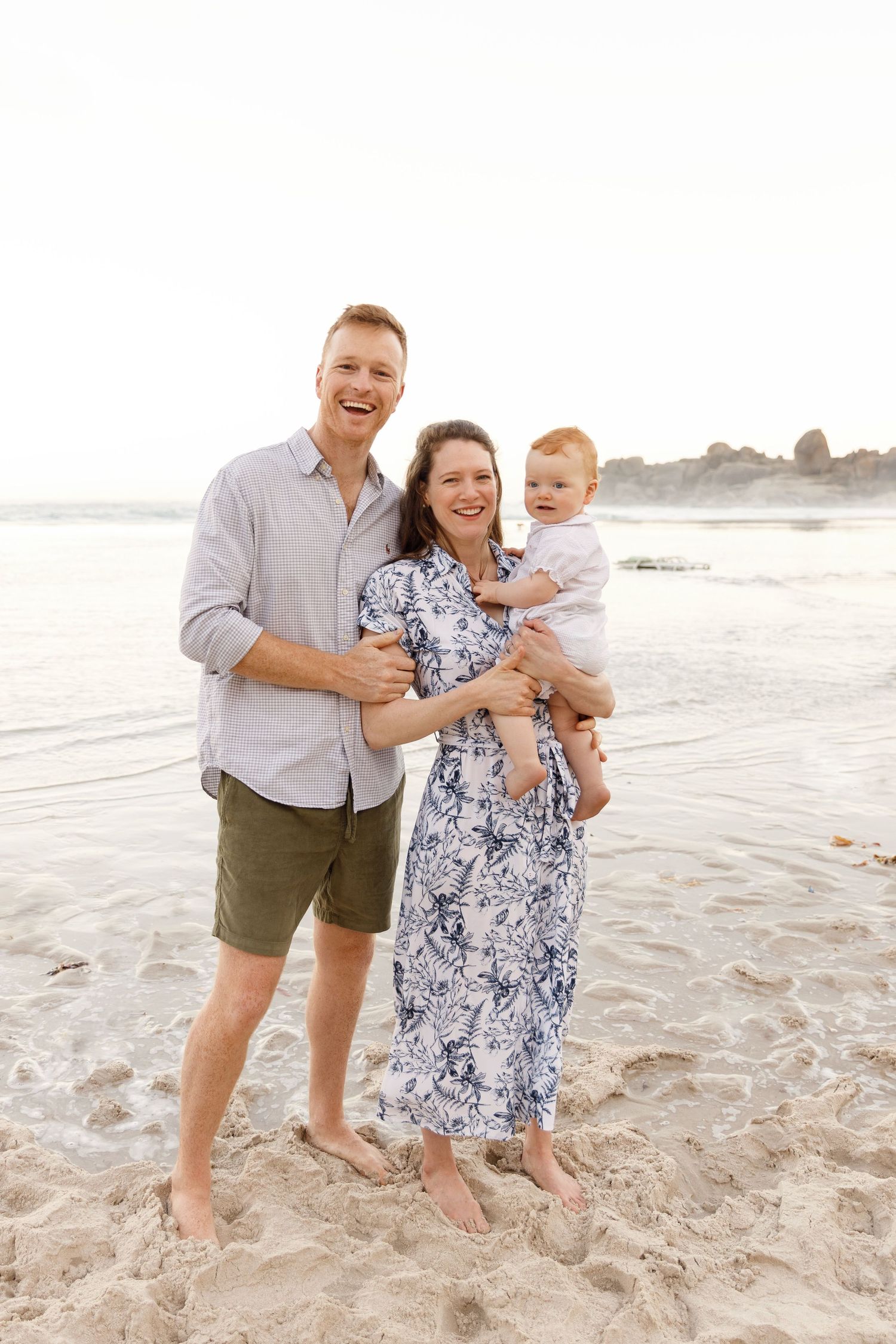 Family enjoying a sunny day together while standing barefoot on a sandy beach at sunset.