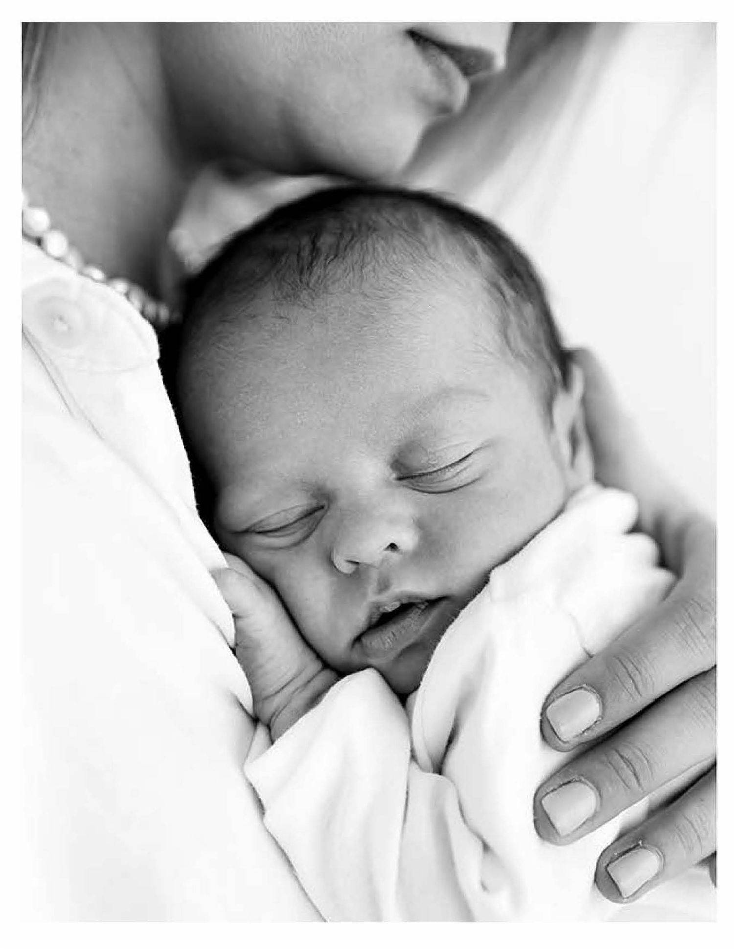 A sleeping newborn baby in black and white photography snuggled close while a hand tenderly cradles them.
